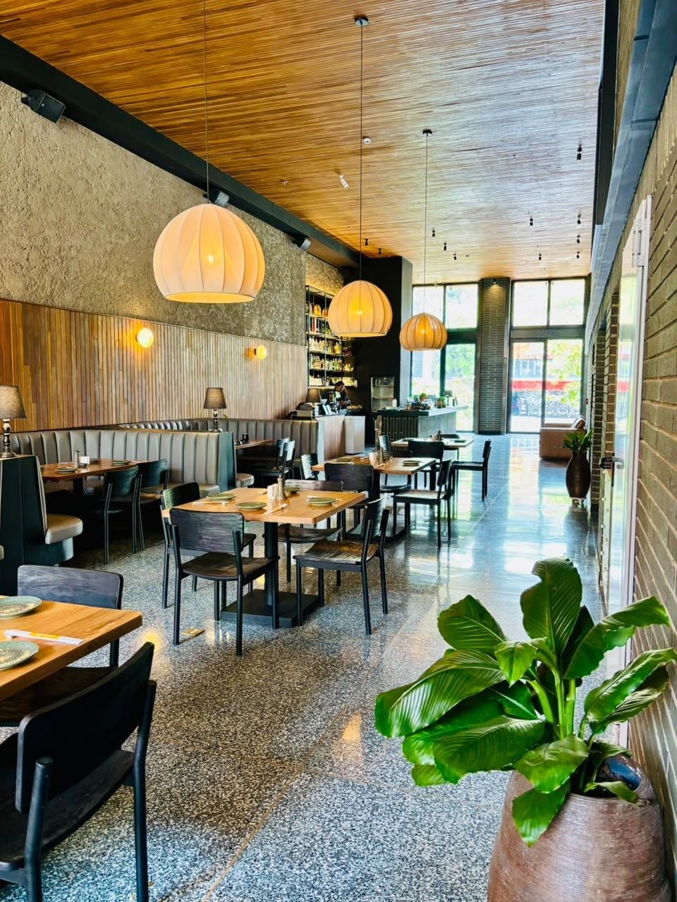 Een restaurantinterieur met houten plafond, tafels, stoelen en hangende吊灯.