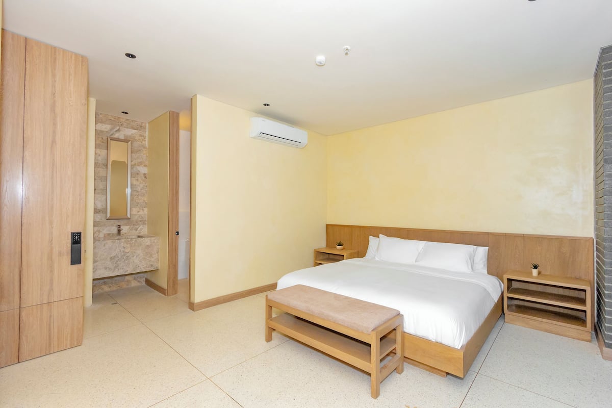 Camera d'albergo moderna con un letto grande, una panca in legno, un comodino e un bagno con parete in pietra e uno specchio.
