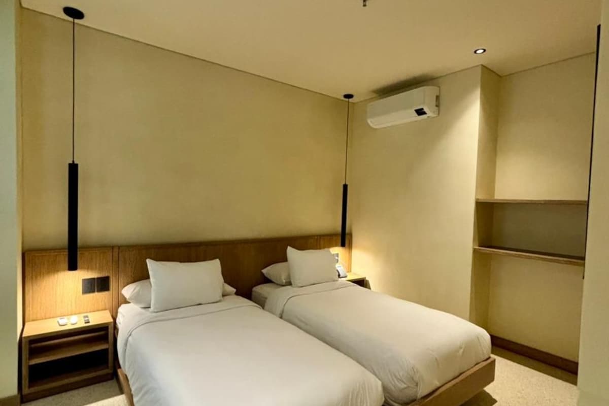 Una moderna camera d'albergo con due letti, un comodino, un condizionatore d'aria a parete e una mensola a incasso.