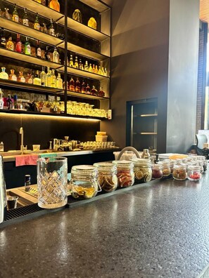 A bar area with shelves of liquor bottles, a countertop with jars of condiments, and a door in the background. - Hotel Iconik (Medellín)