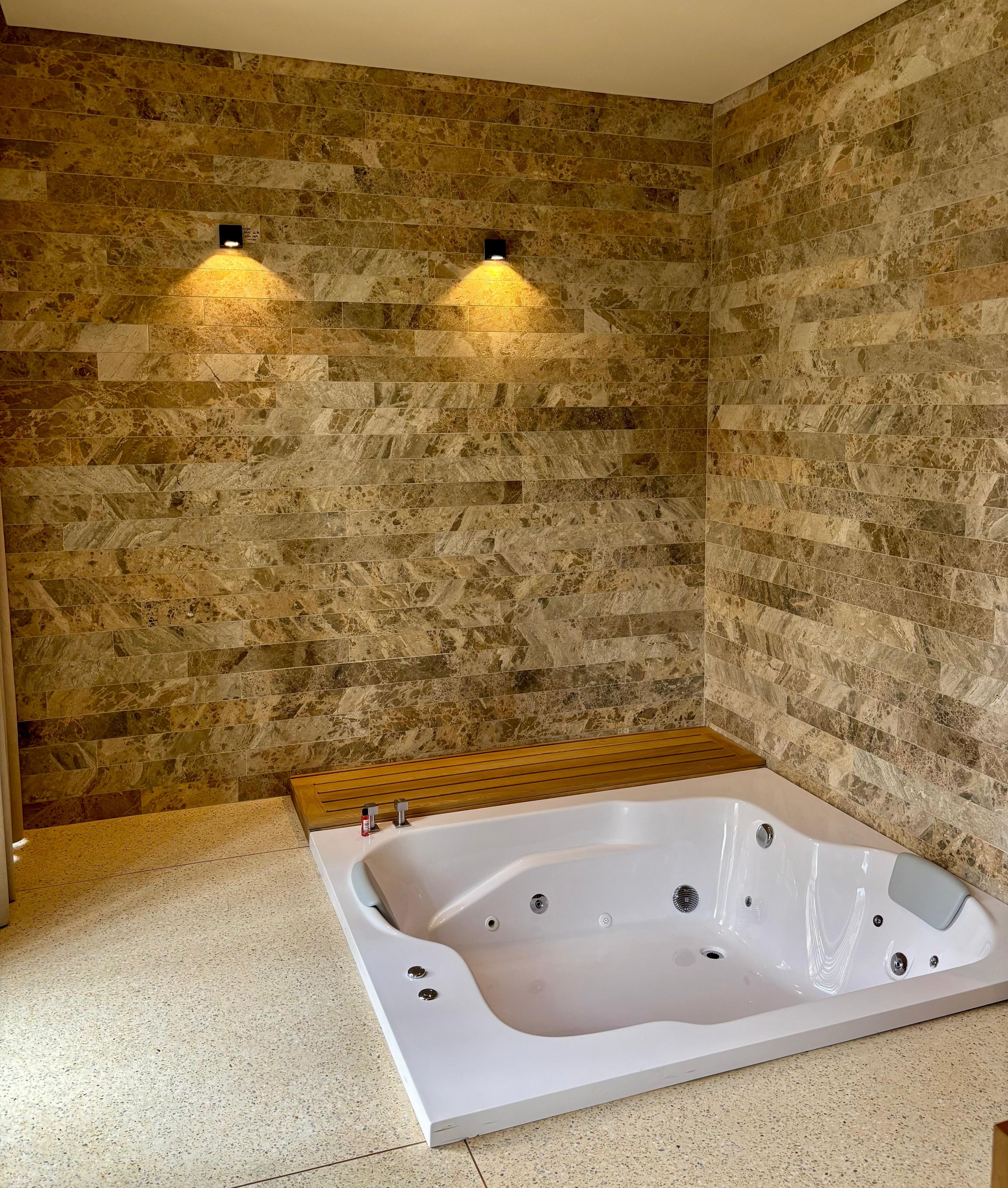 A bathroom with a freestanding bathtub, stone walls, and two wall-mounted lights.