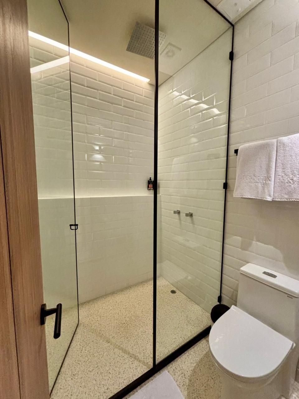 A modern bathroom with a glass-enclosed shower, white subway tiles, a white toilet, and a towel hanging on the wall.