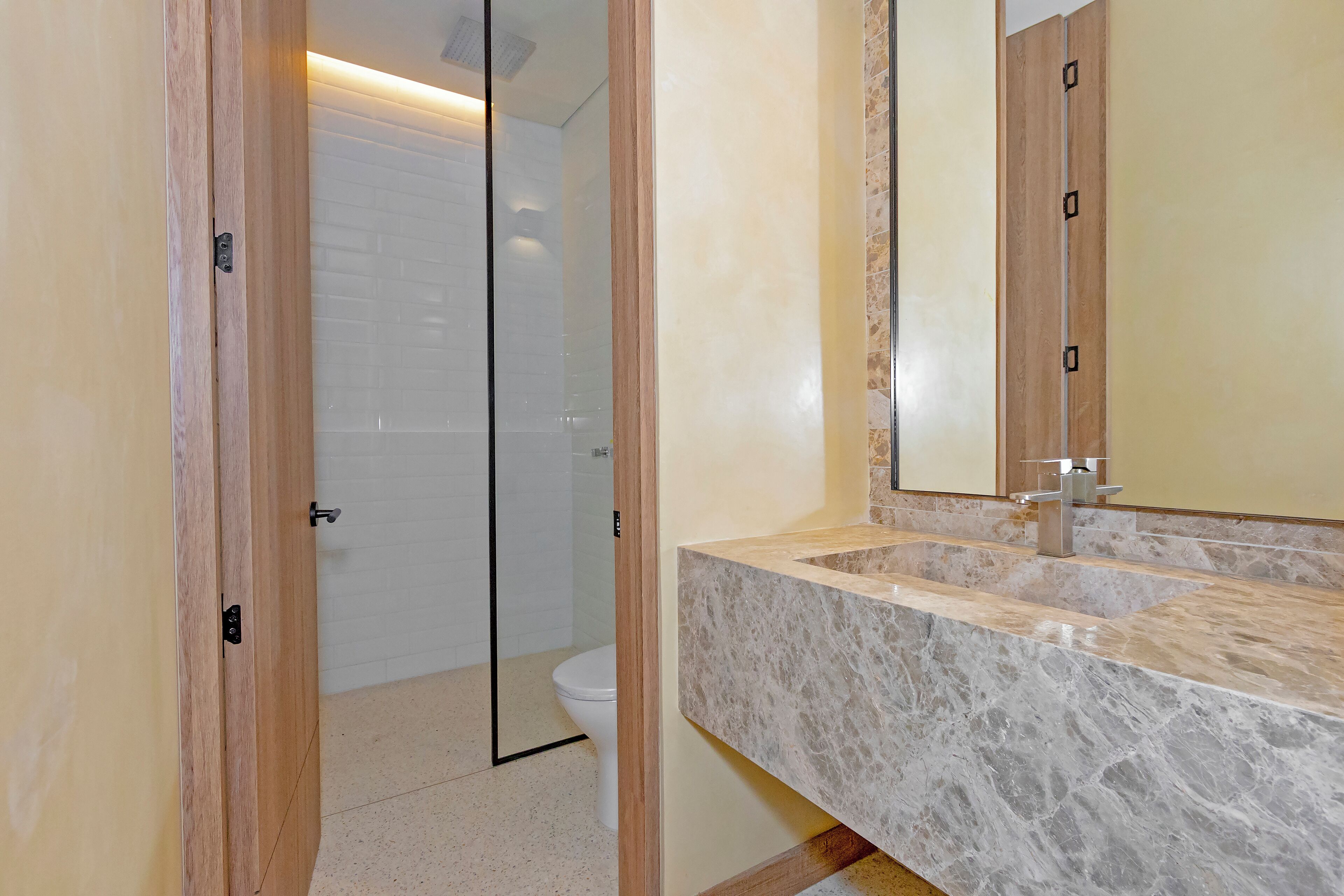 Un baño con lavamanos de mármol, cabina de ducha con paredes de cristal y puertas de madera.