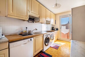 A kitchen with wooden cabinets, a dishwasher, a washing machine, and a window with a view. - Apartment "Accommodation for 4 People" with Private Terrace and Wi-Fi (Nice)