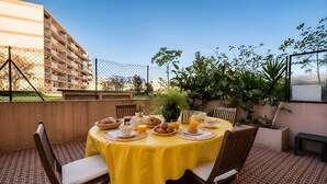 A round table with yellow tablecloth, surrounded by wooden chairs, set outdoors with breakfast items and a clear view of a building in the background. - Apartment "Accommodation for 4 People" with Private Terrace and Wi-Fi (Nice)