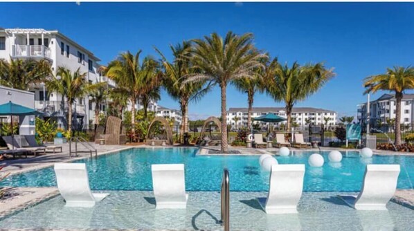 Ein Swimmingpool mit Liegestühlen und Palmen, umgeben von Hotelgebäuden.