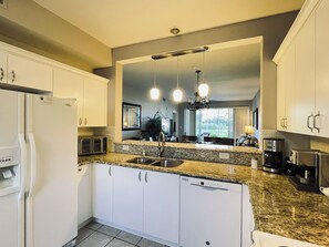 Eine moderne Küche mit weißen Schränken, Granit-Arbeitsplatten, einem eingebauten Geschirrspüler und einer Kaffeemaschine.