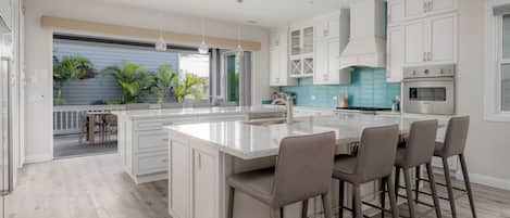 Une cuisine moderne avec des meubles blancs, un grand îlot central doté de tabourets et une vue sur la terrasse extérieure.