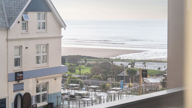 Et strandhotel med udsigt over stranden, udendørs siddepladser og et skilt med teksten 'Tides'.