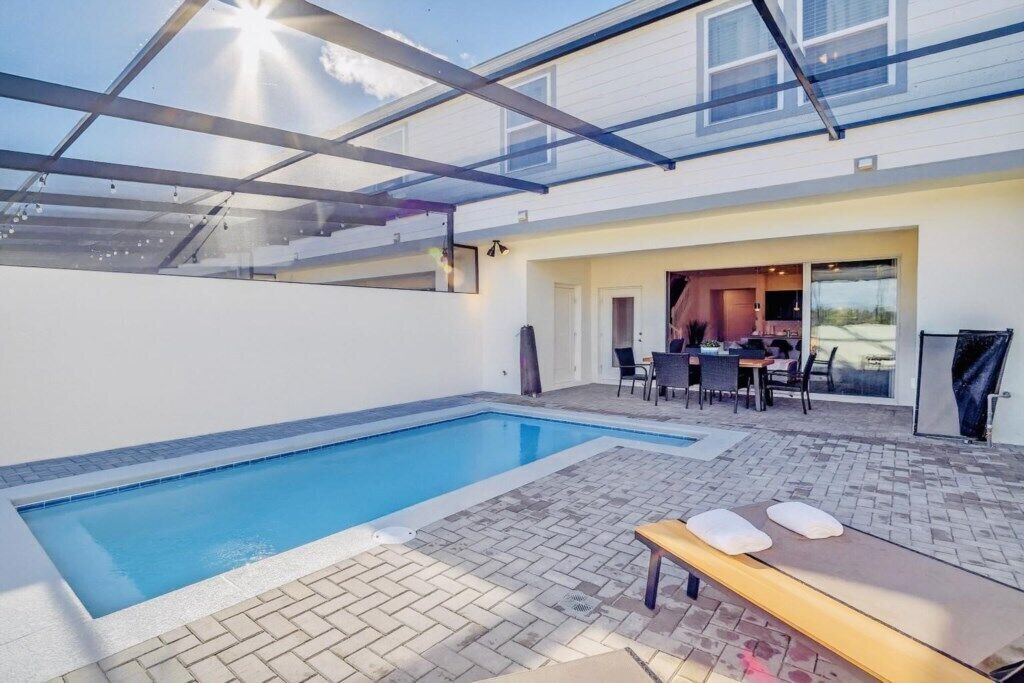 A modern outdoor pool area with a glass ceiling, a lounge chair, and a dining area with outdoor furniture.