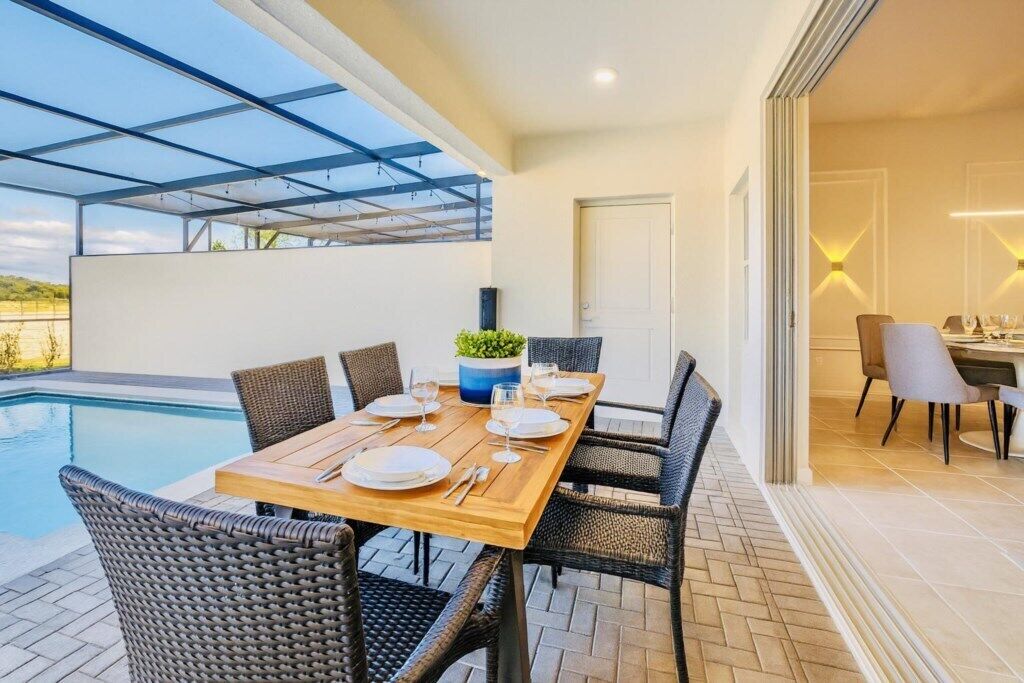 Un coin repas avec vue sur la piscine, une table en bois dressée pour quatre personnes et des chaises en osier.