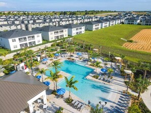 A residential complex with multiple two-story buildings, a central swimming pool with sun loungers, and a landscaped area with palm trees. - ChampionsGate 9BR Retreat | Pool, Spa & Themed Rooms (Davenport)