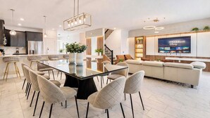 Een moderne keuken met donkere kastjes, een roestvrijstalen koelkast en een eethoek met een glazen tafel en gestoffeerde stoelen.
