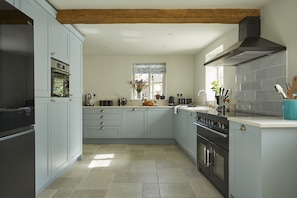 A modern kitchen with light blue cabinets, a central island, stainless steel appliances, and a wooden ceiling beam. - Perfect for large groups. Be it birthdays, wedding parties or a family and friends get-together, we (Bibury)