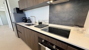 A modern kitchen with wooden cabinets, a black induction cooktop, a stainless steel sink, and a built-in oven. - Studio Vairagi City, brand new in the center of Papeete, WiFi -Netflix -A/C (Papeete)