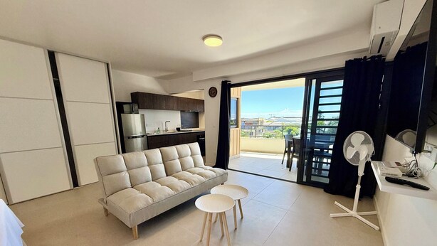 A modern living room with a sofa, two small tables, a fan, and a view of the outside. - Studio Vairagi City, brand new in the center of Papeete, WiFi -Netflix -A/C (Papeete)