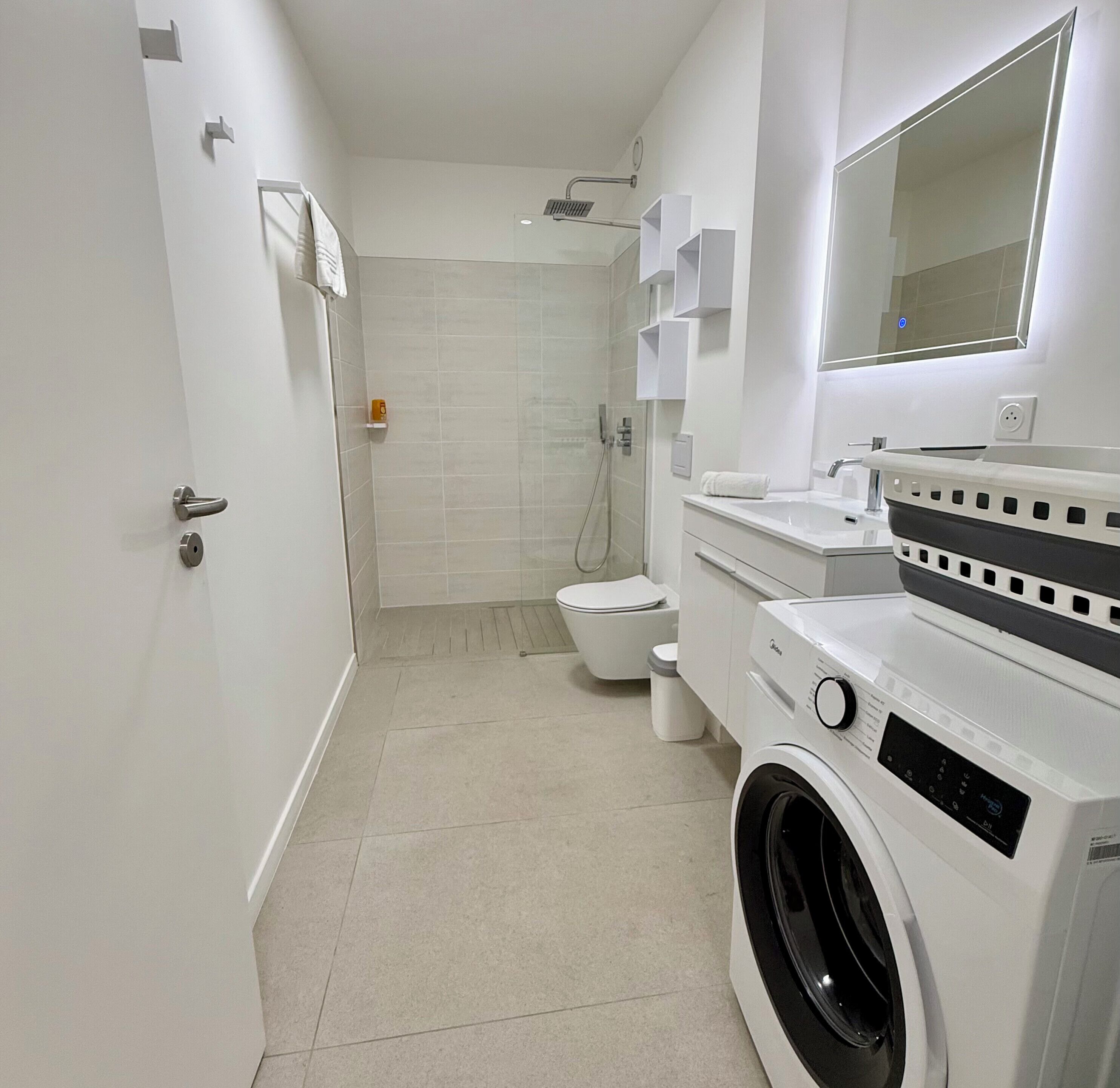 A modern bathroom with a washing machine, toilet, and shower area.