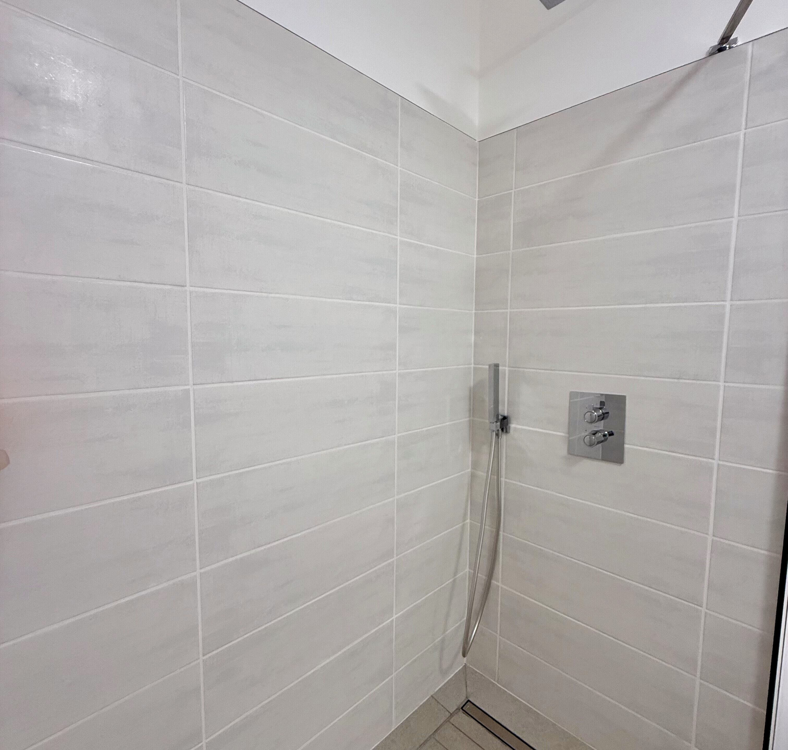 Une douche aux carreaux blancs, une porte en verre et un panneau de commande mural.