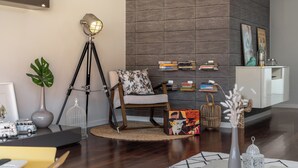 Een moderne woonkamer met een donker houten vloer, een witte fauteuil, een boekenkast en een wandgemonteerde flatscreen-tv.