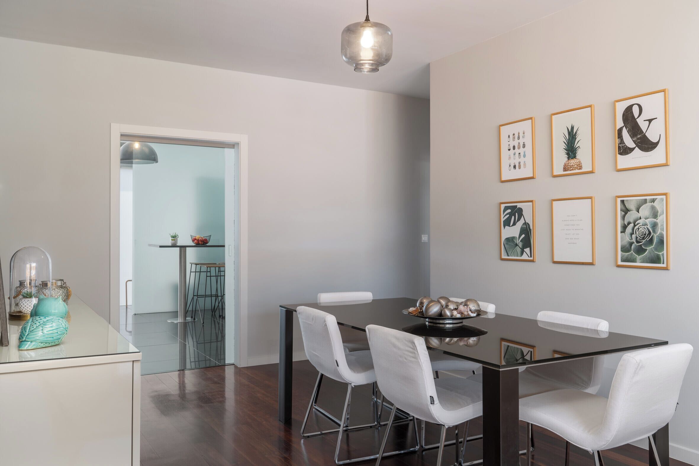Un'elegante zona pranzo moderna con tavolo in vetro, sedie bianche e stampe botaniche incorniciate alle pareti.