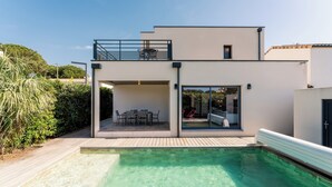 Ett modernt hus i två våningar med en swimmingpool, en balkong med utemöbler och en glasdörr som leder ut till en uteplats.