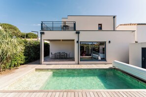 A modern two-story house with a swimming pool, a balcony with outdoor furniture, and a glass door leading to a patio area. - Casano + Azura Dual Villa Near the Beach (Vendres)