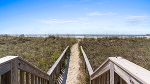 Ein Holzsteg führt zu einem Strand unter blauem Himmel.