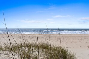 A beach with sand and waves, and some grass in the foreground.