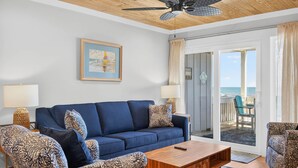 Ein Wohnzimmer mit einem blauen Sofa, gemusterten Sesseln, einem Holztisch, einem Deckenventilator und einem Bild an der Wand.