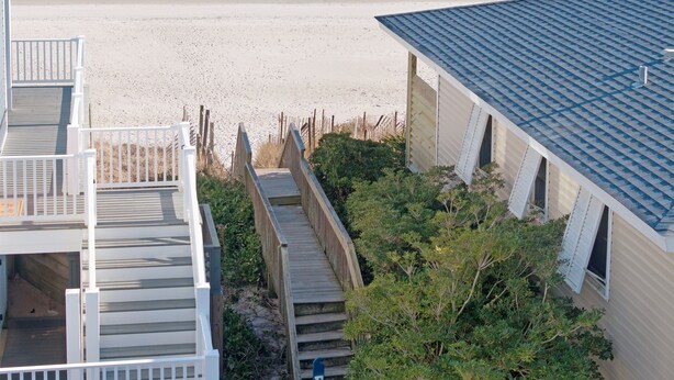 A beach view from a building with a staircase leading to a deck, a sandy beach, and the ocean. - Decks with Ocean Views, Grill, 2 King Suites, Dogs Welcome, 2 Min Walk to Beach (Surf City)