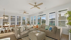 A spacious living room with a large beige sectional sofa, a dining area with white chairs, and a ceiling fan. - Decks with Ocean Views, Grill, 2 King Suites, Dogs Welcome, 2 Min Walk to Beach (Surf City)