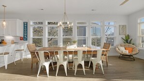 A spacious dining area with a wooden table and white chairs, large windows, and a ceiling fan. - Decks with Ocean Views, Grill, 2 King Suites, Dogs Welcome, 2 Min Walk to Beach (Surf City)