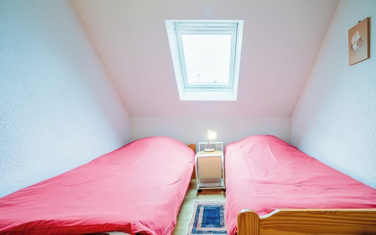 Ein kleiner, gemütlicher Raum mit zwei Einzelbetten, einem Fenster und einem Nachttisch mit Lampe.