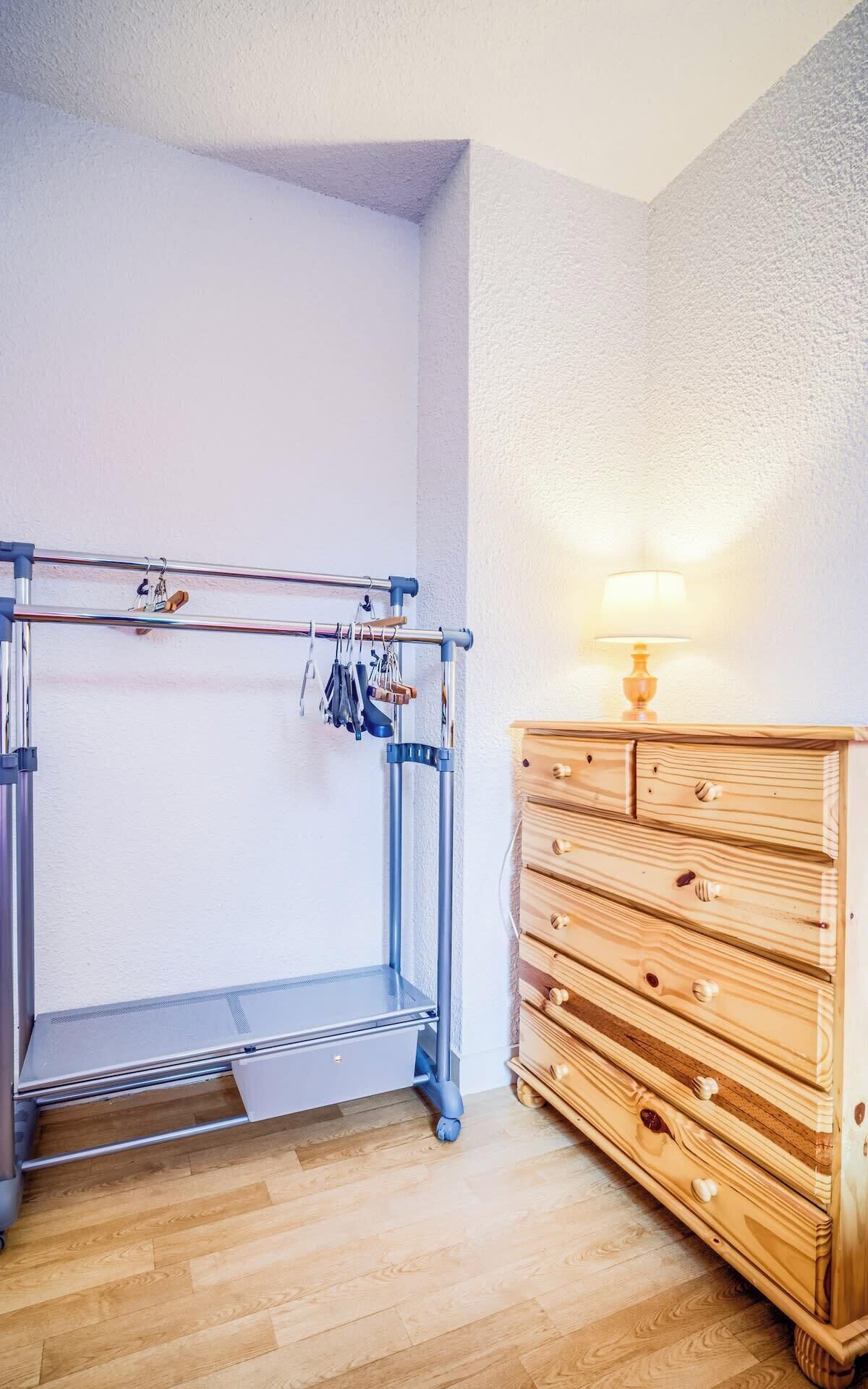 Une pièce comprenant un étendoir métallique, une commode en bois et une lampe.