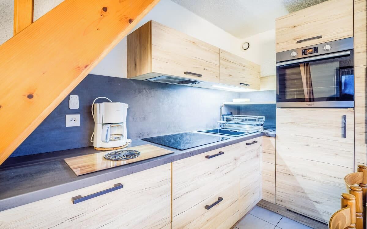 Una cocina moderna con armarios de madera, horno empotrado y cafetera.