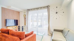 Een moderne woonkamer met een televisie, een oranje bank en een glazen salontafel.