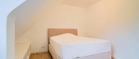 A small, clean room with a single bed, a wooden floor, and a sloped ceiling.