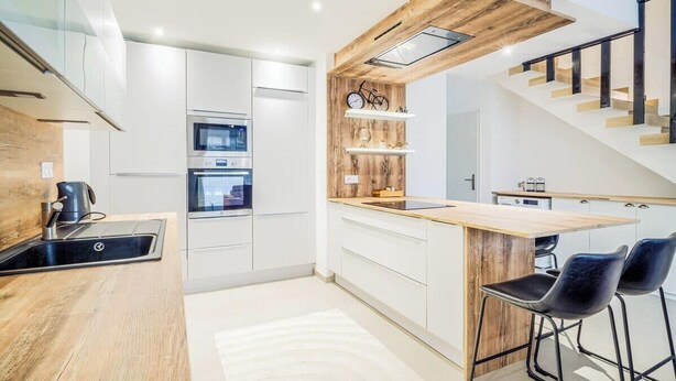 Een moderne keuken met witte kasten, een houten aanrechtblad en een inbouwfornuis. Er is een houten plank met decoratieve objecten en een fiets.