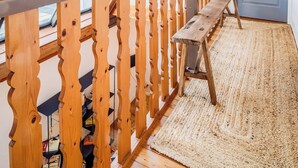 A room with a wooden ceiling, a sloped roof with skylights, a wooden bench, a door, and a woven rug. - Atelier d’Artiste – Ville Close à pied (Concarneau)