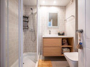 Moderni kylpyhuone, jossa on lasinen suihkuseinä, puinen allaskaappi, wc ja peili pesualtaan yläpuolella.