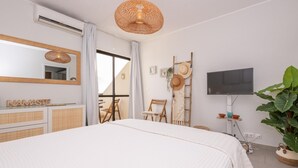 Ein Schlafzimmer mit einem großen Bett, einem Fernseher, einem Balkon mit einem Stuhl und einer Pflanze.