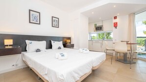 A hotel room with a large bed, a bedside table with a lamp, a small kitchenette, and a view of the outdoors. - 🏖️ White Golden - AC - Wi-Fi - Access Pools & Beach Included (Cabanas de Tavira)