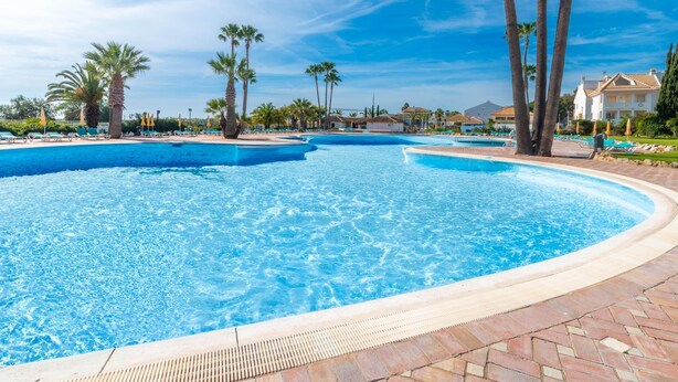 A large, clear swimming pool with palm trees and lounge chairs around it, surrounded by buildings. - 🏖️ White Golden - AC - Wi-Fi - Access Pools & Beach Included (Cabanas de Tavira)