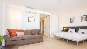 A modern hotel room with a sofa, a bed, a bedside table, and a small table with a plant. - 🏖️ White Golden - AC - Wi-Fi - Access Pools & Beach Included (Cabanas de Tavira)