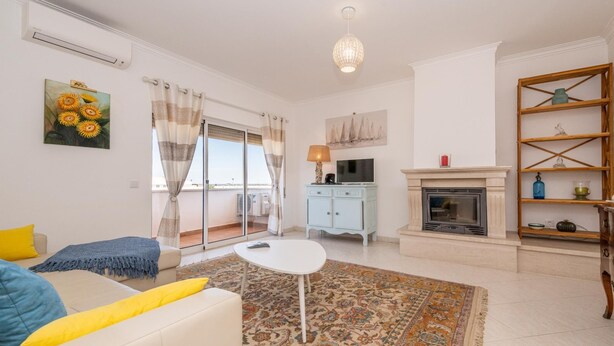 A living room with a sofa, a coffee table, a fireplace, a TV, and a balcony with curtains. - Tavira Getaway with Balcony and Sea View (Tavira)