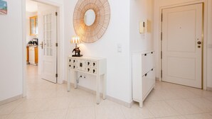 A hallway with a white console table, a round mirror, and a door leading to a kitchen. - Tavira Getaway with Balcony and Sea View (Tavira)
