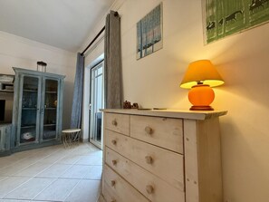 Ein Zimmer mit einem hölzernen Schminktisch, einer Lampe, einem Schrank und einer Tür zu einem weiteren Raum.