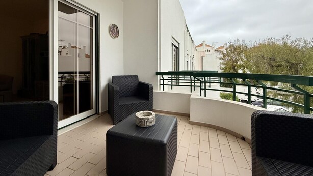 Ein Balkon mit einer Couch, einem kleinen Tisch und einem Stuhl. Eine Glastür führt in einen Innenraum.