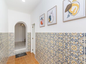 Un couloir orné de carreaux décoratifs, un paillasson et des œuvres d’art encadrées accrochées au mur.