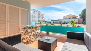Ein Balkon mit einer Couch, einem Esstisch und einem kleinen Couchtisch. Im Hintergrund sind Gebäude zu sehen.